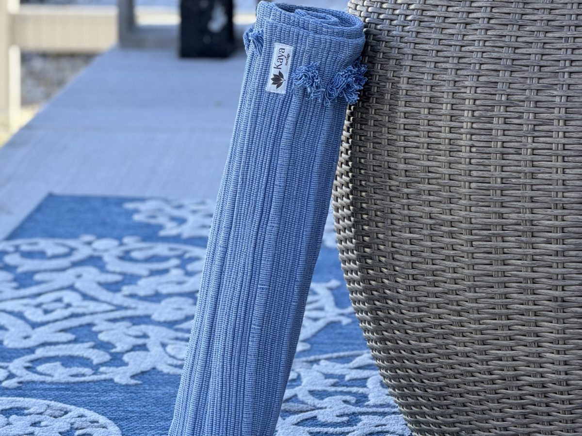 Rolled Vishu Blue organic cotton yoga rug resting on a patio chair outdoors